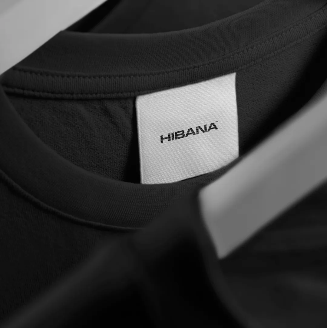 A white Hibana neck label on a dark tee
